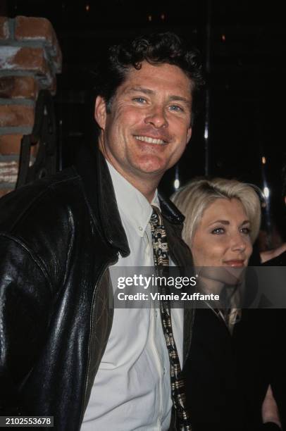 American actor and singer David Hasselhoff, wearing a black leather jacket over a white shirt with a tie, alongside his wife, American actress Pamela...