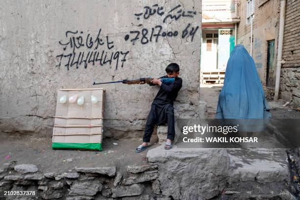 An Afghan burqa-clad woman walks past a boy carrying an airgun in Kabul on March 24, 2024.