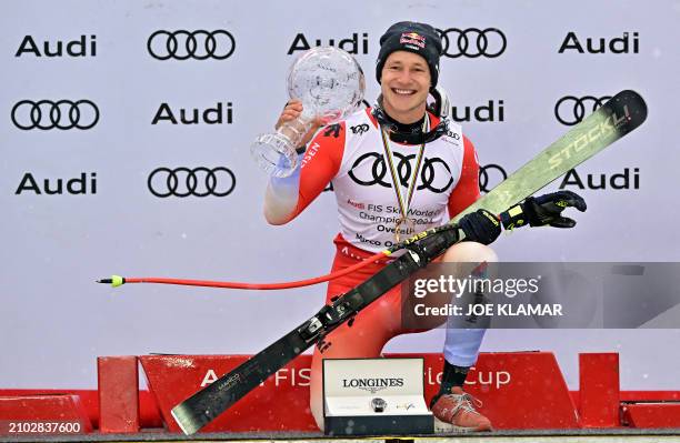 The overall season winner of the Men's FIS Alpine Skiing World Cup Switzerland's Marco Odermatt poses with his trophy on the podium on the last day...