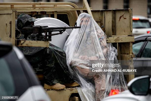 An Iraqi soldier wears a large plastic sheet to protect himself from the heavy rain as he sits in the back of a military vehicle in Baghdad on March...