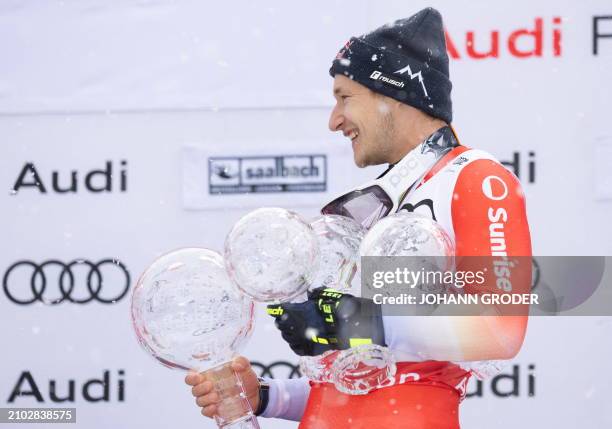 Switzerland's Marco Odermatt holds his trophy globes as he celebrates on the podium after winning the overall season title of the Men's FIS Alpine...