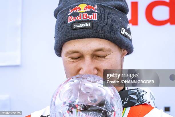 Switzerland's Marco Odermatt kisses his trophy as he celebrates on the podium after winning the overall season title of the Men's FIS Alpine Skiing...
