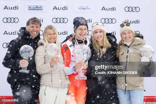 Switzerland's Marco Odermatt holds his big globe trophy as he celebrates on the podium with his parents Walter and Priska as well as his sister Alina...