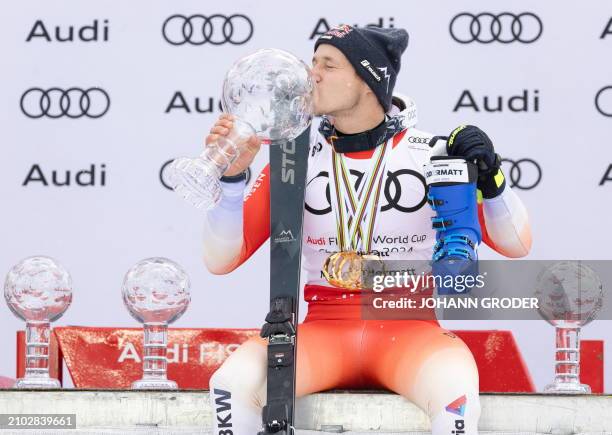 Switzerland's Marco Odermatt kisses his big globe trophy as he celebrates on the podium after winning the overall season title of the Men's FIS...