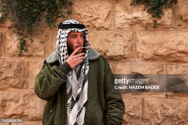 An Israeli settler dressed in Arab garb and wearing a Palestinian keffiyeh headdress as a Purim costume smokes while standing along Al-Shuhada...