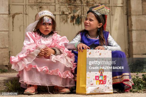 Children dressed in Purim costumes sit on the side of the road along Al-Shuhada street, which is largely closed to Palestinians, in the divided city...
