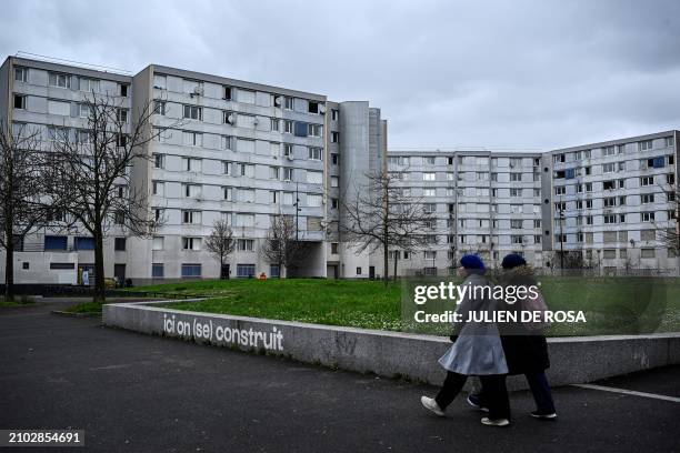 Pedestrians walk past apartment buildings and writting on a wall reading "Here we build " in Le Franc-Moisin neighbourhood of Saint-Denis, a northern...