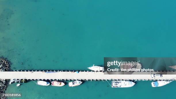 an aerial view of colored boats secured to a single pier at a coastal harbor. - australia jetty stock pictures, royalty-free photos & images