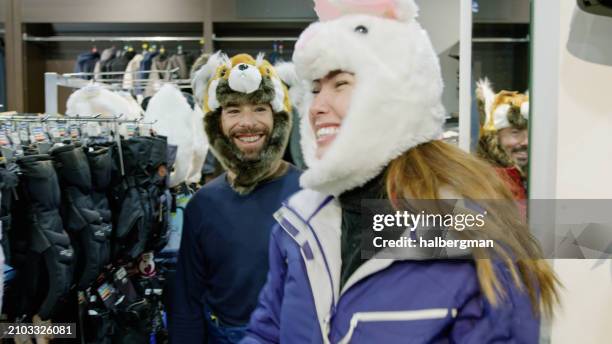 smiling tourists trying on hats in ski store - ski shop stock pictures, royalty-free photos & images