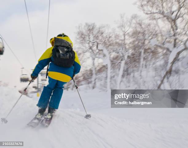 rear view of skier with lift chairs passing overhead in niseko, japan - professional skier stock pictures, royalty-free photos & images