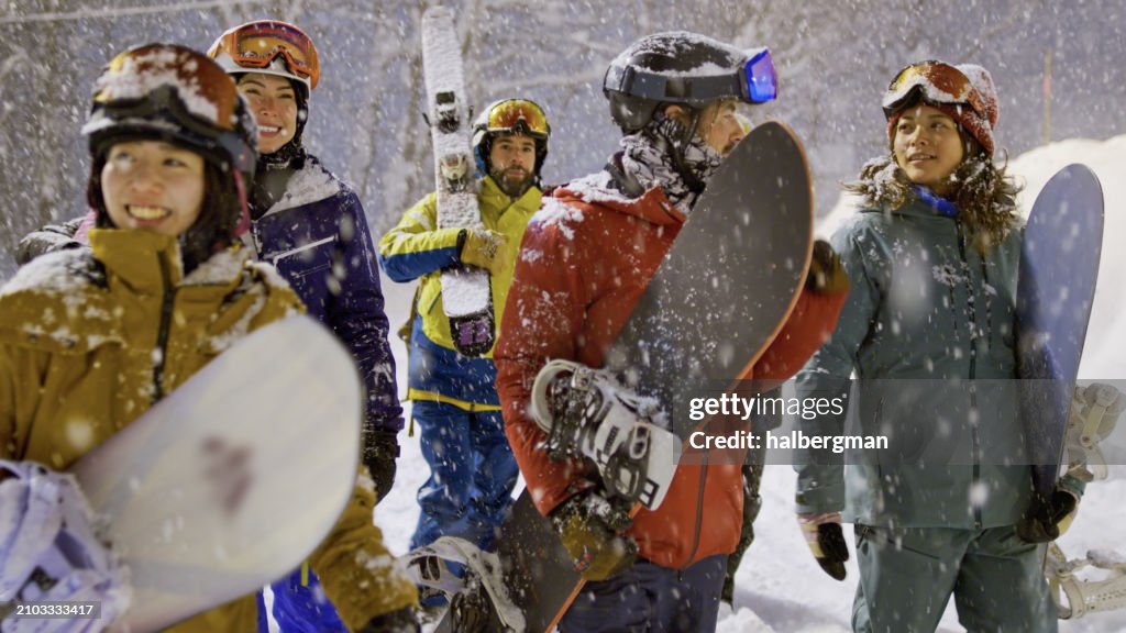 Smiling Skiers and Snowboarders Walking Through Heavy Snow at Night in Niseko