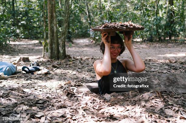 tourist climbs out of a camouflaged exit of a cu chi tunnel - eagle creek trail stockfoto's en -beelden