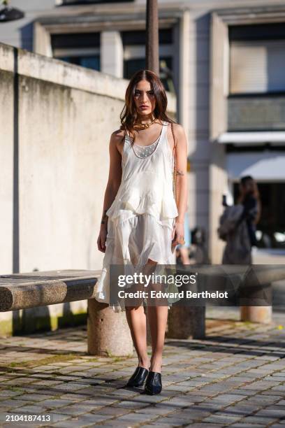 Guest wears a golden necklace, a white sleeveless dress with a handkerchief lower part, black heeled mules, outside Stella McCartney , during the...
