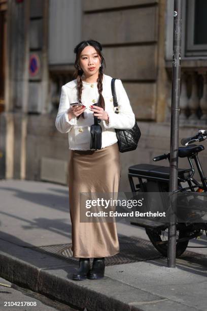 Guest wears a white tweed jacket with brass buttons, a black quilted bag, a bronze satin aspect maxi straight skirt, black shoes , outside Valentino...