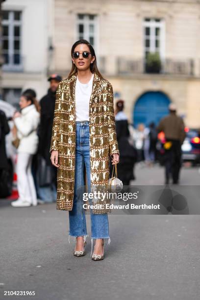 Guest wears sunglasses, a white top, blue denim ripped hem pants, a shiny coat with golden sequins, a sparkly Valentino silver clutch, shiny...