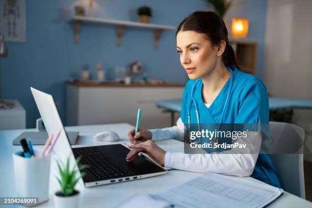 medizinstudentin in blauem kittel, e-learning auf einem laptop bei der ordination - medizinische dokumente stock-fotos und bilder