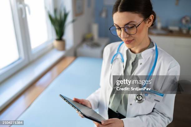 junge kaukasische ärztin mit digitalem tablet bei der ordination - ordination stock-fotos und bilder