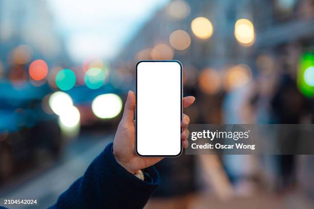 female hand holding smartphone with blank screen against city light bokeh - mobility as a service stock-fotos und bilder