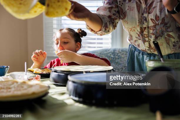 tasty homemade crepes. hungry girl eating pancakes as her mother cooks nearby. - tasty stock pictures, royalty-free photos & images