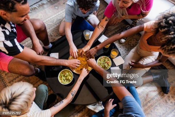 jóvenes amigos comiendo guacamole con nacho en casa - salsa espesa fotografías e imágenes de stock