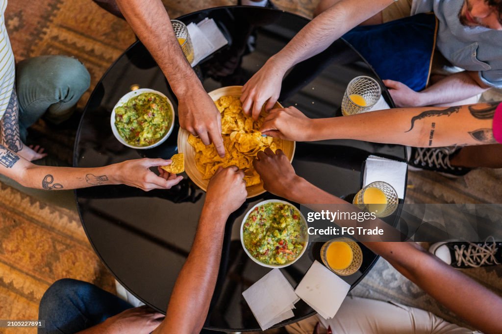 Friends eating guacamole with nacho at home