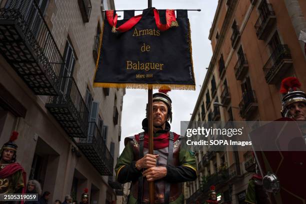 Man dressed as a Roman carries a banner that says "Armats de Balaguer" during the procession of the Good Death. Procession of the Good Death was...