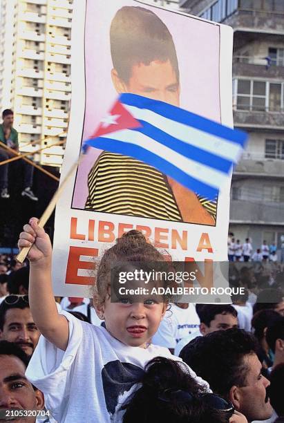 Cuban child holds a flag 10 January 2000 in front of a poster in Havana of Elian Gonzalez who is in Miami, FL pending his return to Cuba. Una nina...