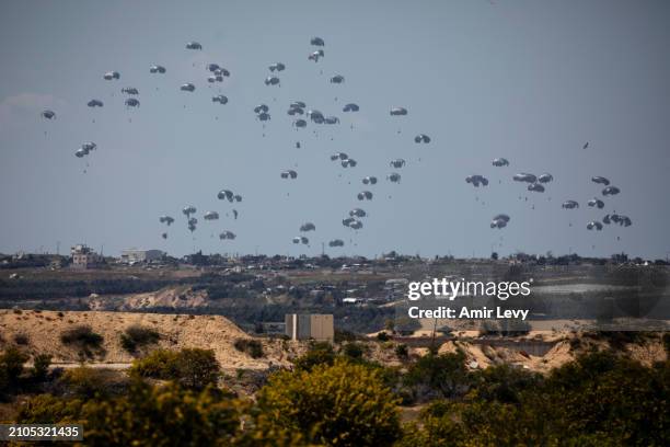 Humanitarian aid falls through the sky toward the Gaza Strip as seen from a position on the Israeli side of the border on March 25, 2024 in Southern...