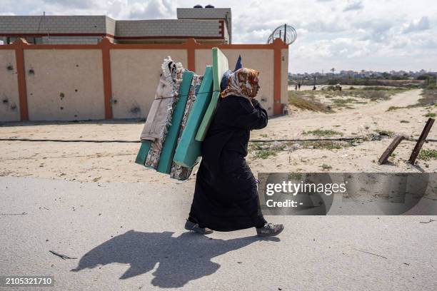 Woman walks with foam mattresses, rugs, and pillows while evacuating from Gaza City on March 25, 2024 amid the ongoing conflict in the Palestinian...