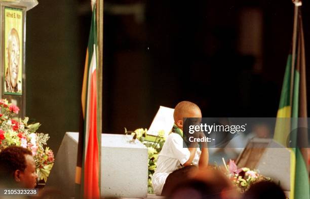 Mthunzi Nzo sits 22 January 2000 on the podium next to a poster of his grandfather, former South African Foreign Minister Alfred Nzo, during his...
