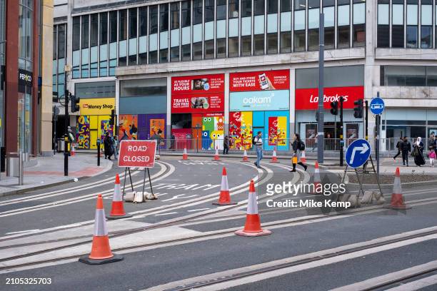 People walking between traffic cones around a junction during the construction site on the update to the Midland Metro tram public transport system...
