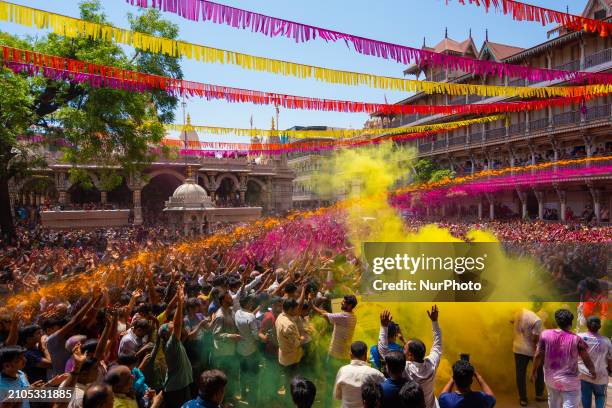 Thousands of devotees are cheering as a priest sprays colored powder and water on them during the celebrations of the colorful Holi festival at the...