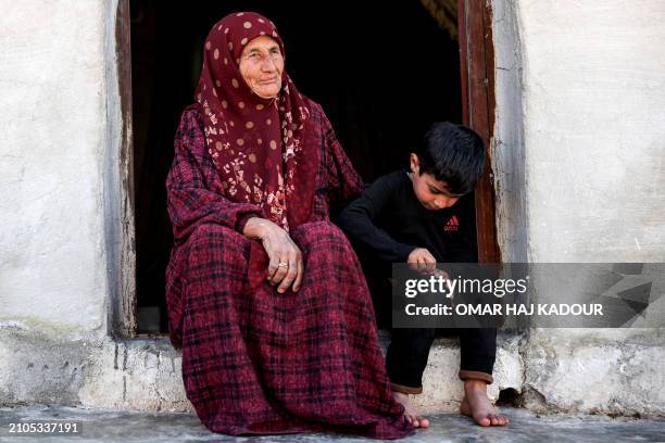 Amina al-Hamam whose son Ghazwan Hassun was detained by Hayat Tahrir al-Sham in 2019, sits with her grandson at the entrance of their tent at a camp...