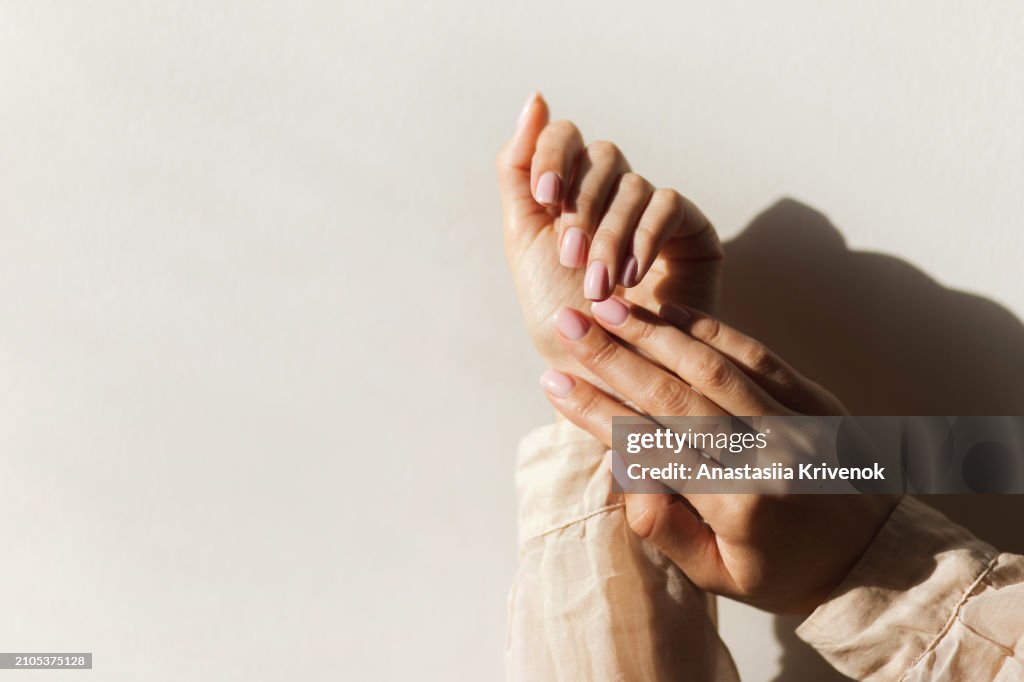 Manicure on female hands with light pink nail polish.