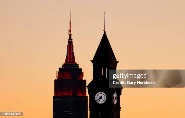 The Empire State Building in New York City still lit in red for a Star Wars promotion the previous night, stands next to the Lackawanna Clock Tower...