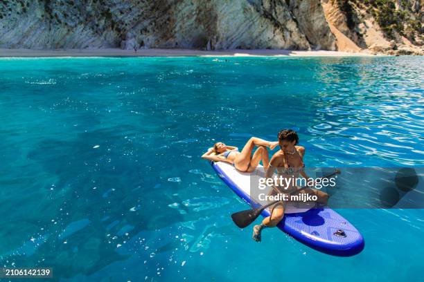 two attractive young woman on a paddleboard in sea - paddleboard stock pictures, royalty-free photos & images