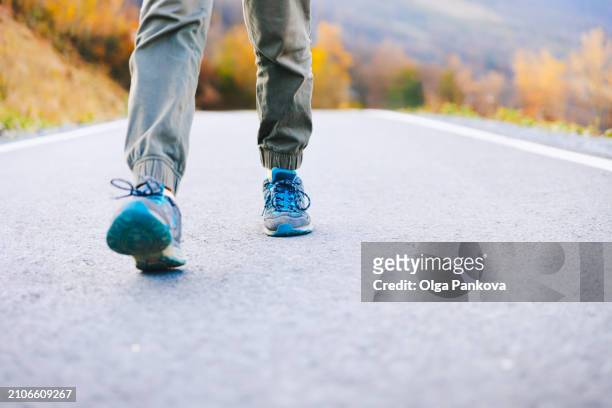 hiker's feet in close-up on the road with sneakers on an autumn background - shoe boot stock pictures, royalty-free photos & images