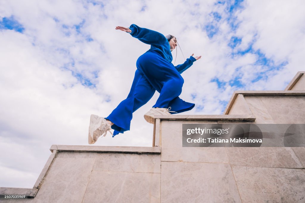 A young woman in blue suit running up the stairs on blue sky background. View from below.
