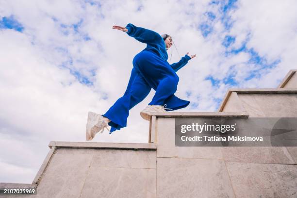 a young woman in blue suit running up the stairs on blue sky background. view from below. - walking to the sky photos et images de collection