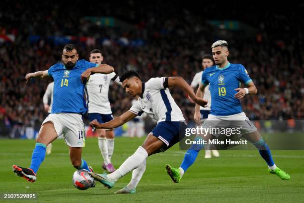 Ollie Watkins of England crosses the ball whilst under pressure from Fabricio Bruno and Andreas Pereira of Brazil during the international friendly...