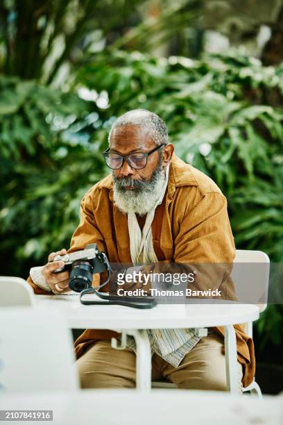 medium wide shot of senior man looking at photos on camera at café - cream colored pants stock pictures, royalty-free photos & images