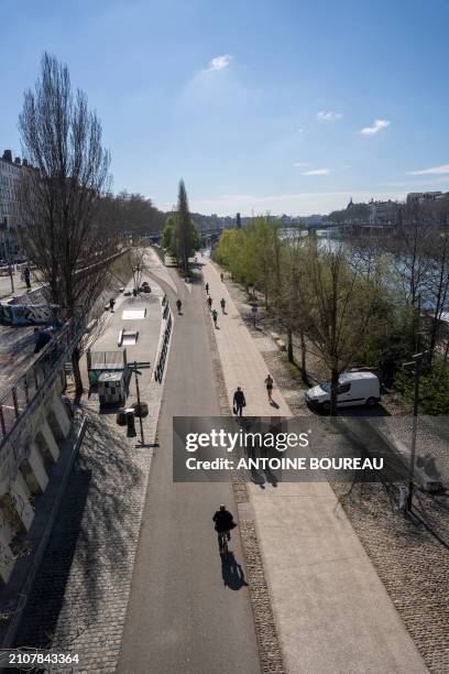 Cyclists and joggers on the cycle path and pedestrian walkway on the Quai du Rh?ne under a blue sky and text space in Lyon, France on 19 March 2024.