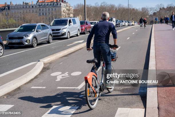 Man seen from behind riding a Velov on a cycle path on the Pont Morand in Lyon, France, on 19 March 2024.