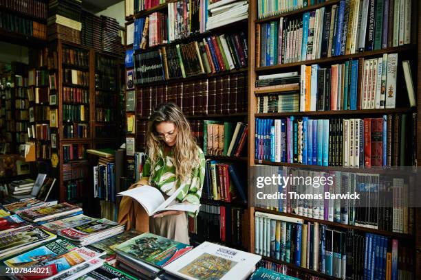 medium wide shot woman reading book while browsing in antique bookstore - libreria foto e immagini stock