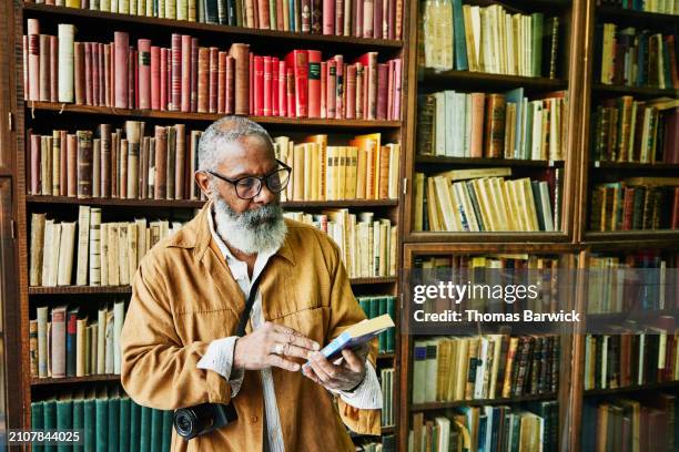 medium wide shot senior man browsing books in antique bookstore - wide shot person looking at the camera - fotografias e filmes do acervo