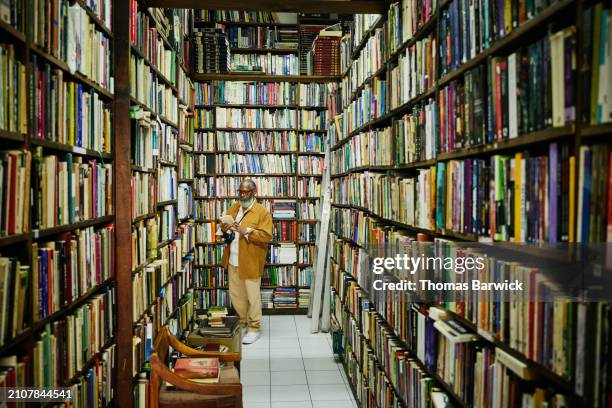 wide shot senior man browsing in antique bookstore during city vacation - large group of objects stock pictures, royalty-free photos & images