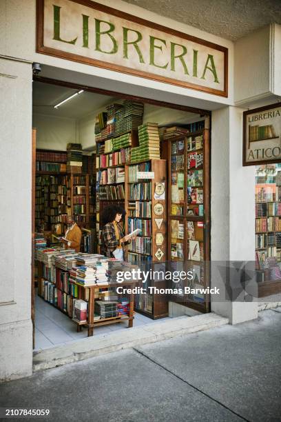 wide shot woman reading book while browsing in antique bookstore - book shop stock pictures, royalty-free photos & images