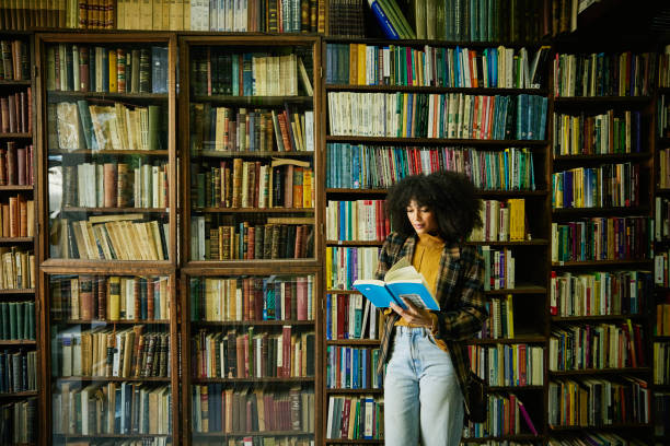 wide shot woman reading book while browsing in antique bookstore - books stock pictures, royalty-free photos & images