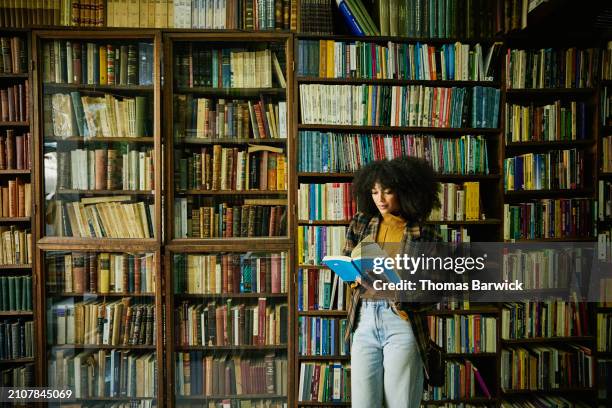 wide shot woman reading book while browsing in antique bookstore - book library stock pictures, royalty-free photos & images