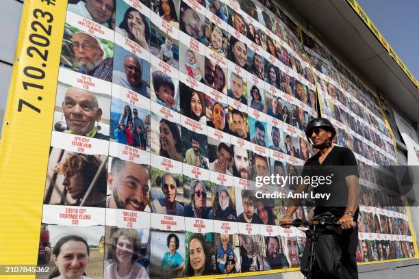 Man passes by a building covered with photos of hostages who have been released or are still being held in the Gaza Strip, on March 26, 2024 in Tel...